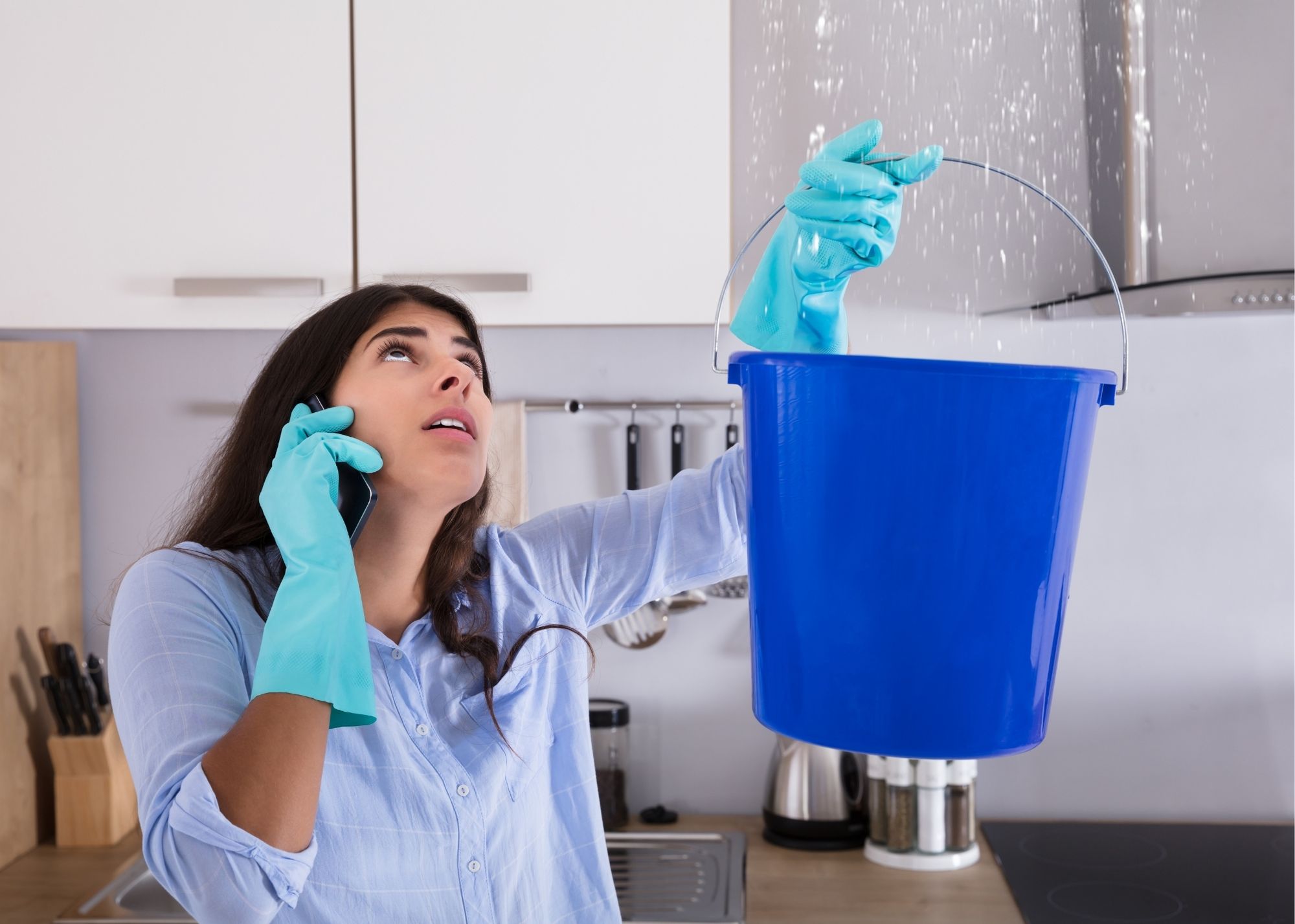 A bucket catching a ceiling leak while a homeowner calls for help in a Rivergate home in Edgewater, FL
